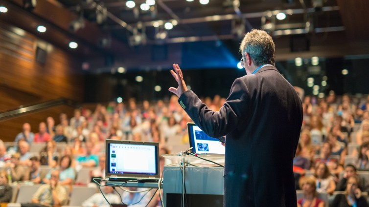 Man spreekt mensen in een zaal toe