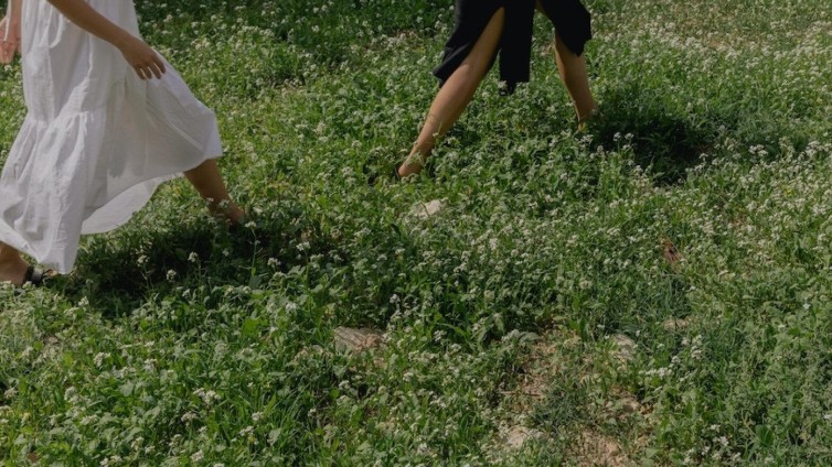 Twee personen lopen met blote benen door een groen weiland vol bloemen