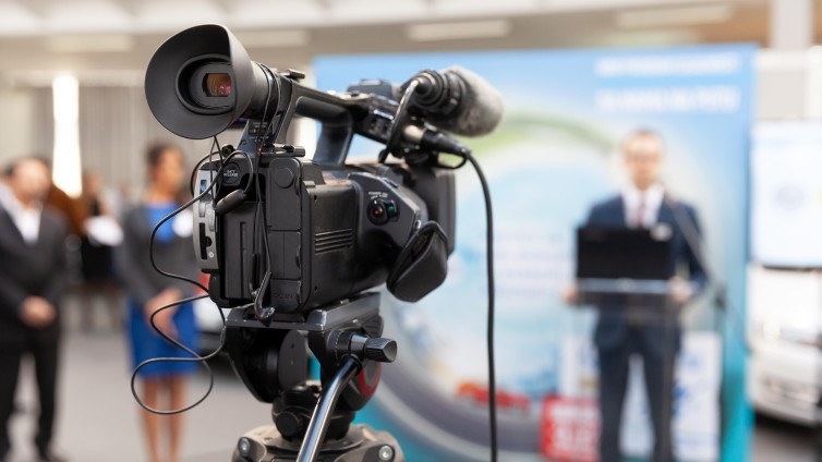 een camera staat gericht op een zakelijk spreker in een zaal