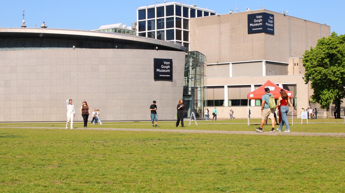 Gebouw van het Van Gogh Museum met logo's en mensen op het grasveld ervoor bij zonnig weer.