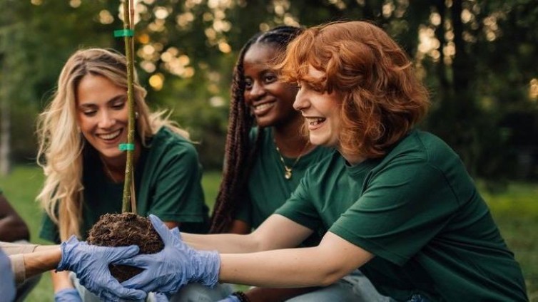 Jonge vrijwilligers planten samen een boom tijdens een groene activiteit in de buitenlucht.